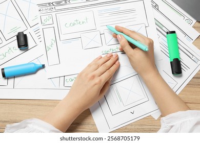 Website designer creating wireframe on paper with pen at wooden table, top view