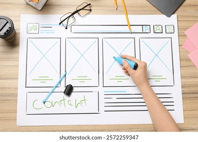Website designer creating wireframe on paper with highlighter at wooden table, top view