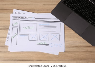 Website development. Sketches of wireframes and laptop on wooden table, flat lay