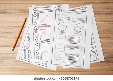 Website development. Sketches of wireframes and pencil on wooden table, flat lay