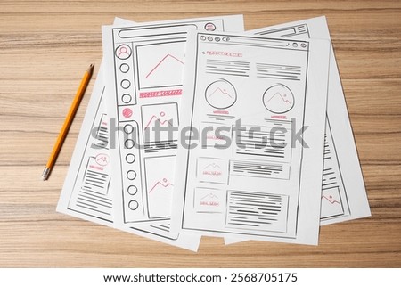 Website development. Sketches of wireframes and pencil on wooden table, flat lay