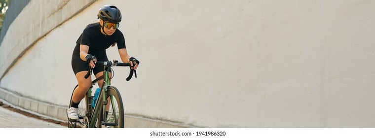 Website Header Of Professional Female Cyclist In Black Cycling Garment And Protective Gear Riding Bicycle In City While Training Outdoors On A Daytime