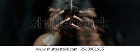 Website header shot through glass with water running down of depressed Black man covering head with hands, hiding face in deep shadows casting from contrast top light in studio with black background