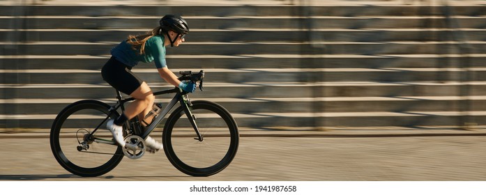 Website header of Side view of professional female cyclist in cycling garment and protective gear riding bicycle in city, rushing and passing buildings while training outdoors on a daytime - Powered by Shutterstock