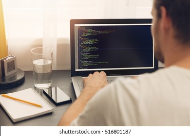 website programmer working on laptop at office. php website code on screen. Visible translations for page titles -Production, Project management, Partners and Contacts in Latvian and Russian languages
