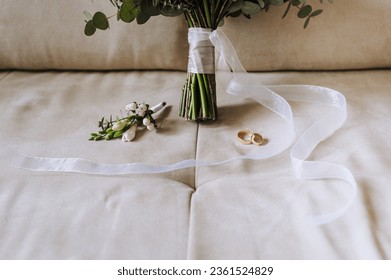 Wedding accessories and details, gold rings, a beautiful bouquet of flowers with a ribbon lie on a beige sofa. Close-up photography, portrait. - Powered by Shutterstock