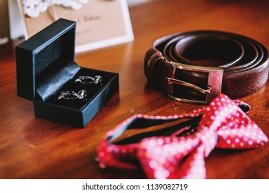 Wedding accessories. A red bow tie, a brown leather strap, black and silver cufflinks lie on a wooden table. - Powered by Shutterstock