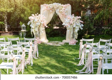 Wedding arch decorated with cloth and flowers outdoors. Beautiful wedding set up. Wedding ceremony on green lawn in the garden. Part of the festive decor, floral arrangement.