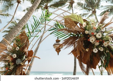Wedding Arch Decorated With Flowers For Beach Ceremony Against The Sea Landscape. Tropical Wedding Ceremony In Boho/ Rustic Style
