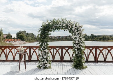 Wedding arch decorated with white flowers at the background of the river. Outside wedding ceremony place