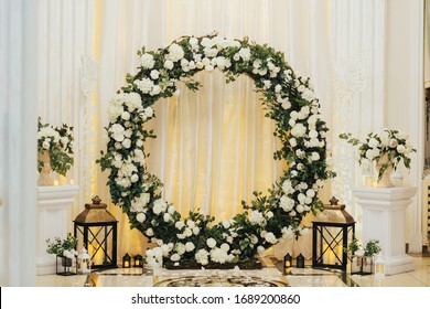 Wedding arch at the restaurant. Round flower arch. Trend in the wedding banquet room is a white  arch decorated with flowers and greens, in the background white cloth.