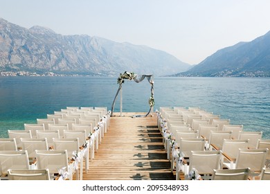 Wedding arch stands in front of a row of chairs on a wooden pier overlooking the mountains - Powered by Shutterstock