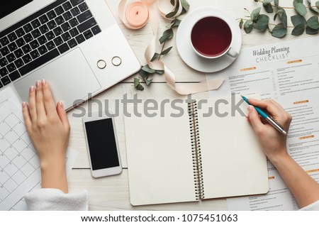 Wedding arrangement background. Female hands preparing for marriage, using laptop, smartphone, paper calendars and planners, top view. Bridal wallpaper with copy space on to do list