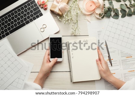 Wedding arrangement background. Female hands preparing for marriage, using laptop, smartphone, paper calendars and planners, top view. Bridal wallpaper with copy space on to do list