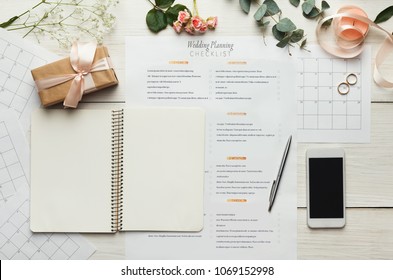 Wedding Background With Checklist. Paper Planner And Wedding Rings On White Wooden Table With Lots Of Tender Bridal Stuff, Top View