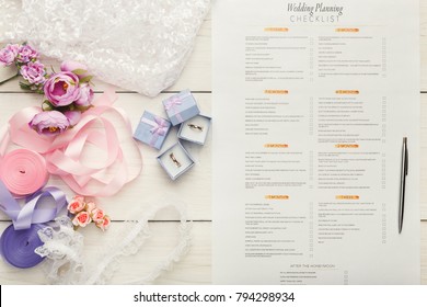 Wedding background with checklist. Paper planner and wedding rings on white wooden table with lots of tender bridal stuff, top view