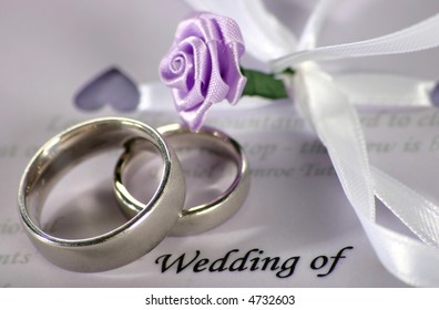 Wedding Bands Sitting On Wedding Invitation/program With Decorative Flowers