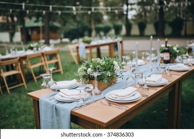 Wedding. Banquet. The chairs and table for guests, decorated with candles, served with cutlery and crockery and covered with a tablecloth. The table stands on a green lawn in the backyard banquet area