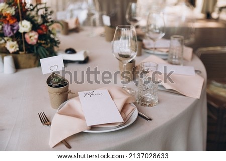 Wedding banquet. The festive table is decorated with compositions of flowers and greenery. On the table are glasses, talers with napkins, cutlery and name cards and menu cards.