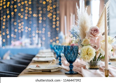 Wedding Banquet or gala dinner. The chairs and table for guests, served with cutlery and crockery. Covered with a pastel pink tablecloth runner. party lighted with garlands