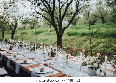 Wedding banquet table in a garden decorated with a composition of white flowers and greenery, there are cutlery and candles - Powered by Shutterstock