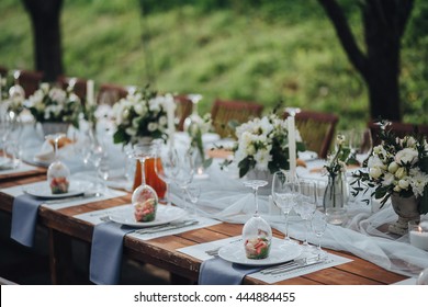 Wedding banquet table in a garden decorated with a composition of white flowers and greenery, there are cutlery and candles - Powered by Shutterstock