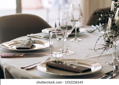 Wedding Banquet Table Setting. Plates, Glasses, Cutlery And Flower Arrangement On A White Round Table. Round Table With A White Tablecloth. Plate With A Gray Cloth Napkin.