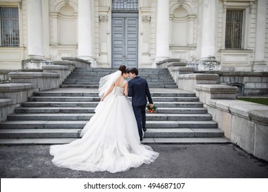 Wedding in a beautiful location. Wedding couple,bride and groom holding hands and going up the stairs of the castle. Elegant wedding dress with a long train