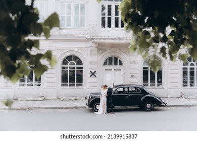 Wedding of a beautiful, stylish couple, a bride in a white wedding dress and a groom in a black suit, tuxedo, in a black retro car.