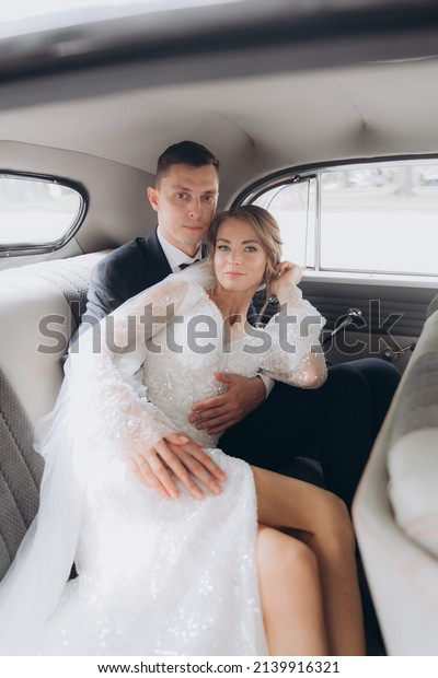 Wedding of a beautiful, stylish couple, a bride in a\
white wedding dress and a groom in a black suit, tuxedo, in a black\
retro car.