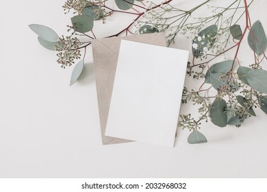 Wedding, birthday stationery composition. Blank greeting card, invitation mockup and craft envelope. Green Eucalyptus populus branches, Gypsophila flowers isolated on table background. Flat lay, top. - Shutterstock ID 2032968032