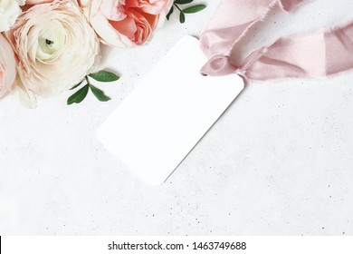 Wedding, Birthday Stationery Mock-up Scene. Blank Gift Tag, Label With Pink Silk Ribbon. Decorative Floral Corner. Green Leaves, Pink English Rose And Ranunculus Flowers. Concrete Table Background. 