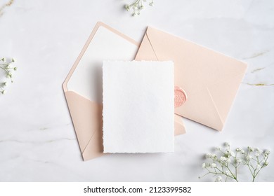 Wedding Blank Card And Pink Envelopes With Gypsophila Flowers On Marble Table. Flat Lay, Top View.