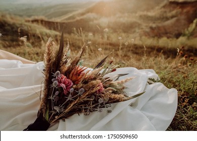 wedding bouquet in boho style collected from wild flowers, the bride holds a bouquet in her hand, in nature, white dress, live plants, a composition of dried flowers