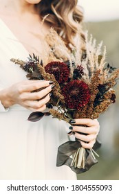 Wedding Bouquet In Boho Style On The Background Of Nature. The Bride Holds A Bouquet Of Dried Flowers.