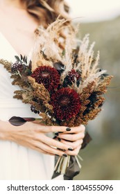 Wedding Bouquet In Boho Style On The Background Of Nature. The Bride Holds A Bouquet Of Dried Flowers.