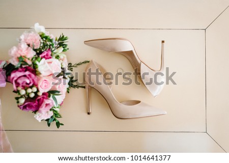 Wedding bouquet of the bride of pink flowers roses and greens, stylish elegant classic lacquered beige shoes and two silver wedding rings lying on pastel background. Close up. flat lay. top view.
