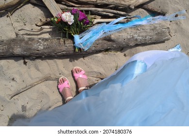 
The Wedding Bouquet Lies On A Log. Feet In Sonoids And Polol Dress Against A Background Of Sand