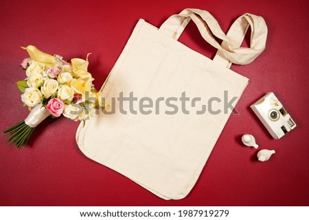 Wedding and bridal party theme canvas tote bag SVG craft product flat lay mockup on modern maroon red background.