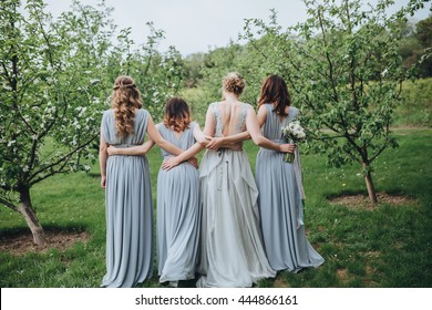 Wedding. The bride in a white dress standing and embracing bridesmaids in green garden