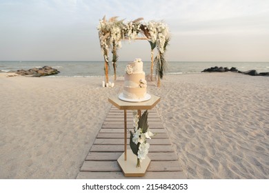 Wedding cake at a beach wedding on the background of a beautiful arch for an exit ceremony. - Shutterstock ID 2154842053