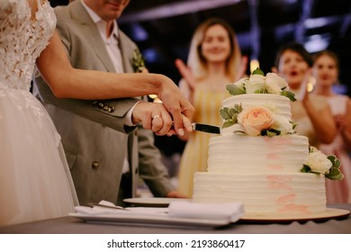 The wedding cake. The bride and groom cut off a piece of cake with a knife. The hands of the newlyweds cut the first piece of the wedding cake. Close-up photo.