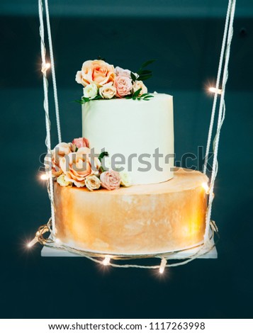 Wedding cake on decorative swing, decorated with fowers and luminous garland