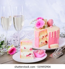 Wedding cake with pink frosting and white chocolate ganache, decorated with flowers and macaroons. Wedding gown in the background - Powered by Shutterstock