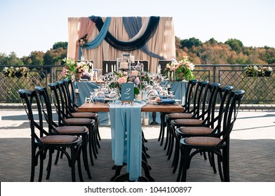 Wedding catered event setting, flowers, candles, white plates, blue napkins, wooden tables, Event decoration, outdoors, summer time