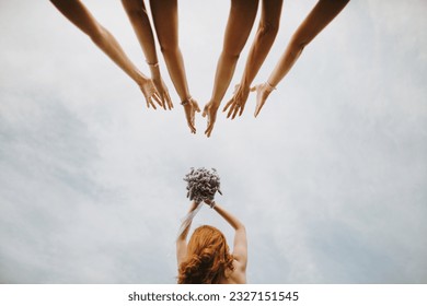 Wedding celebration. Bridesmaids catching bridal bouquet of flowers. Wedding tradition. Red hair bride dropping bridal bouquet and bridesmaids try to catch it
