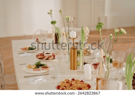 Wedding celebration table set with assorted appetizers, glassware, candles, and floral arrangements, elegant food presentation on plates, transparent chairs surrounding decorated table
