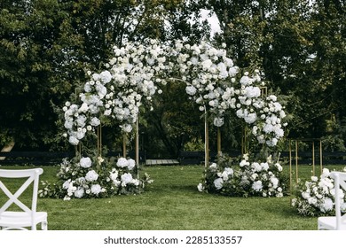 Wedding ceremony aisle with an arch decorated with flowers placed on green grass. Garden wedding venue.