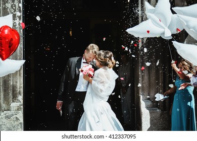 Wedding ceremony. Bride and groom embracing near church  and smiling. A lot of flowers, confetti and balloons. Guests around. Outdoor