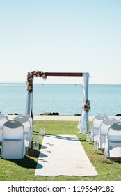 Wedding Ceremony On The Beach With Flower Adorned Wooden Wedding Arbor And White Chairs